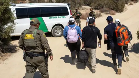 Getty Images US Border Patrol officers take migrants into custody after they crossed the US-Mexico border. 