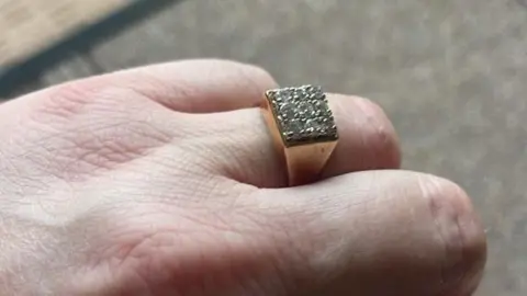 A man's hand with a gold ring set with diamonds on his wedding finger. 