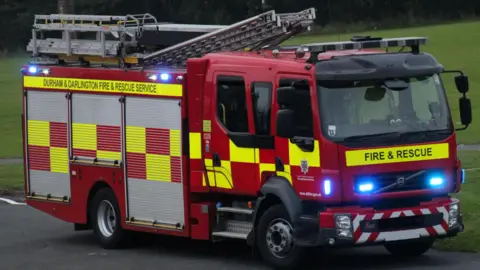 A County Durham and Darlington Fire and Rescue Service engine. The red and yellow vehicle's lights are flashing.