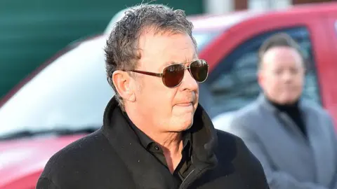 PA Media Shane Richie wearing a black coat and sunglasses