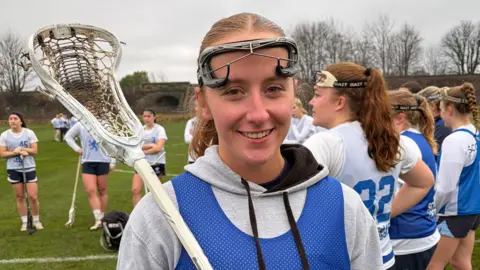 Woman holds a white lacrosse stick and wears a blue Team Scotland kit