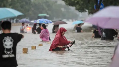 Getty Images This photo taken on July 20, 2021 shows people wading through flood waters along a street following heavy rains in Zhengzhou