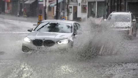 Getty Images A car driving through a flooded section of road