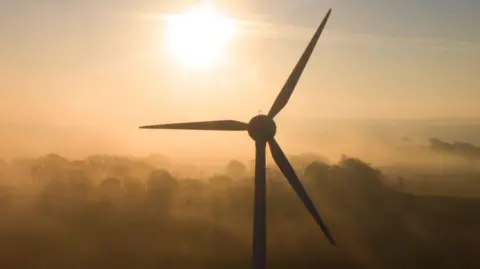 A wind turbine on a misty day at sunset