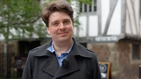 Benjamin Alborough in a double breasted coat stood in a Leicester street.