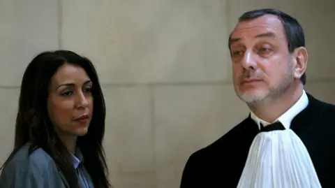 AFP via Getty Images A woman in blue and with long black hair on the left stands beside a man in French legal clothing