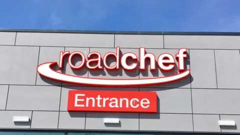 Front view of a red and white Roadchef sign. An additional sign that reads "Entrance" is mounted below.