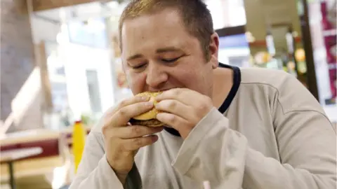 Science Photo Library Man eating fast-food burger
