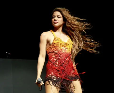 Getty Images Shakira on stage in a short red and yellow dress with shoulder straps