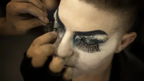 A make-up artist applies fake eyelashes to Elias