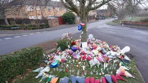 PA Media Floral tributes and candles at a tree