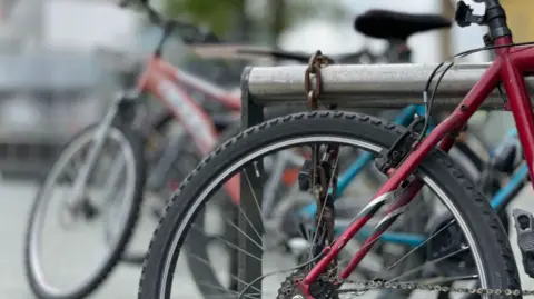 A mainly red bike with a black wheel is parked. Other bikes are blurred in the background.