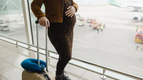 stock image of a pregnant woman with suitcase at an airport