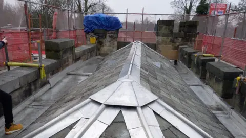 A small sloped roof with grey tiles and fencing surrounding it
