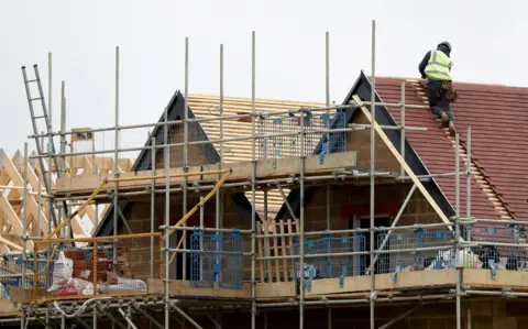 A generic housebuilding image showing a builder on a roof and scaffolding.