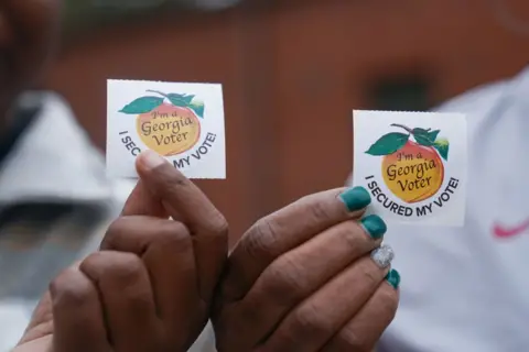 Megan Varner/Getty Images Voters hold up their stickers after visiting a polling place to cast their ballots on 5 November 2024 in Atlanta, Georgia