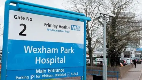 Blue and white NHS sign with the words 'Wexham Park Hospital' outside the hospital building