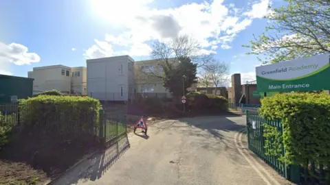 LDRS The outside of Greenfield Academy, which has green gates and white buildings.