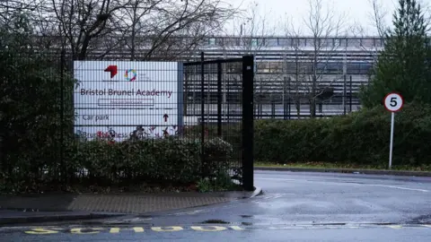 Press Association The gates of Bristol Brunel Academy. The word "School" is painted in yellow on the road in front of the black fence. The gates are open with a 5mph sign on the grass. The school sign is white with burgundy writing. 