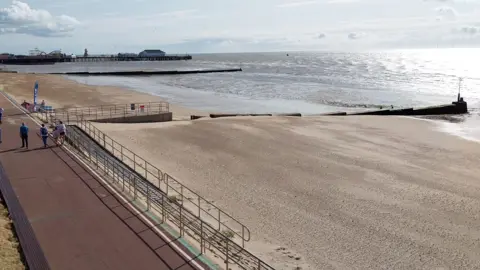 Owen Ward/BBC A view of a beach from above. The promenade is on the lefthand side, and the sandy beach and the sea is the to the right. The pier is in the background.