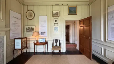 The National Trust A room with white walls, a big oak door and various paintings on the wall.