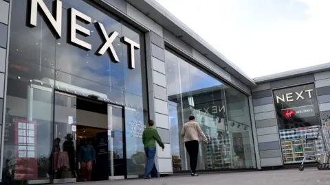 A Next store is seen with the logo looming large over passers-by as they walk outside the storefront on a sunny-cloudy day in Basildon in October.