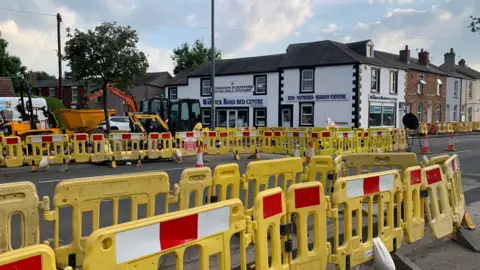 BBC/Billy Hotchkiss Yellow bollards block a section of a road in Carlisle, with diggers carrying out work in the distance.