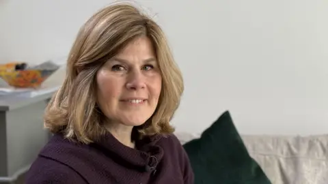 Cristiana Jones Caccavale in a purple jumper sitting on her sofa. 