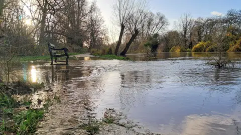 A stretch of the towpath between Port Meadow and Botley Road flooding over a towpath, with a bench on the left side.
