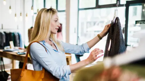 Getty Images Woman holding up an item of clothing while shopping