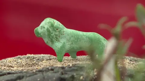 A green lion playing piece on sand.