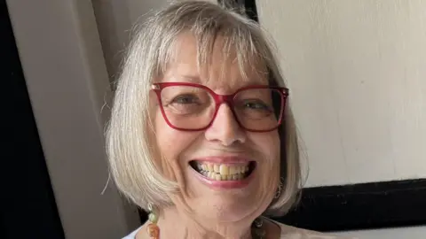 Irene Bates Irene Bates has light coloured hair in a bob style, she has pink framed glasses and is smiling, behind her is a white internal wall.