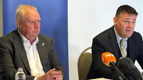 Alan Savage, wearing a white shirt and grey suit jacket, sits with James Stephen, wearing a shirt tie and suit, during the Inverness Caley Jags press conference.