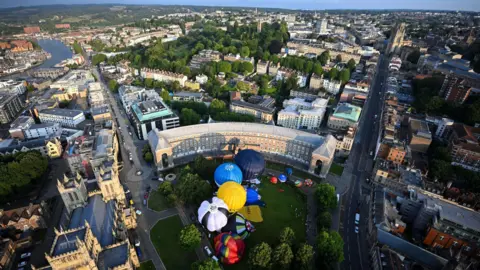 Getty Images A cluster of colourful hot air balloons are seen from the air on College Green in the centre of Bristol. The image also shows a large part of the city in the background including Park Street and the harbourside.