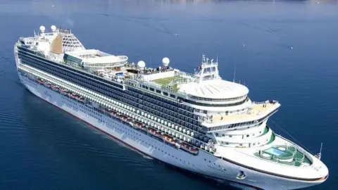 P&O Ventura cruise ship in sea, from bird's eye view. Photographed on a clear sunny day. Some passengers could be seen on board. There are smaller vessels near it.