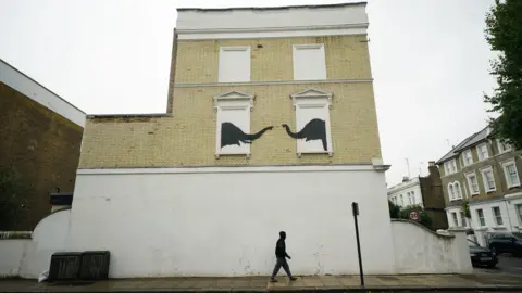 PA Media Banksy artwork depicting two elephants reaching out to one another from building's false windows