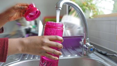 A hand filling up a clear pink plastic water bottle in the tap
