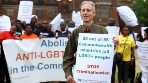 Reuters Peter Tatchell stands holding a banner that reads '35 out of 56 Commonwealth countries jail LGBT+ people'. People holding banners stand behind him.