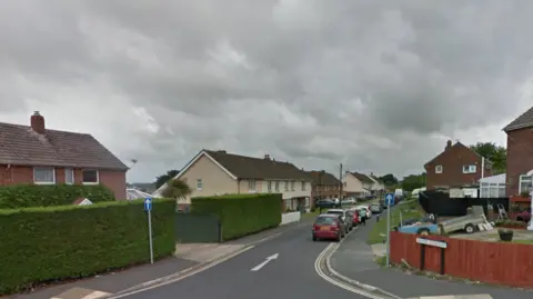 A general view picture of Manor Crescent in Newport on the Isle of Wight. It is a residential area with cars parked on one side of the road, with houses on either side.