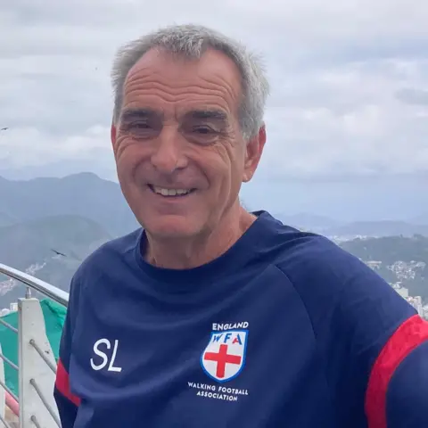 Stuart Langworthy Stuart Langworthy has short white hair and is smiling. He is wearing a blue football top with England Walking Football Association written on it.