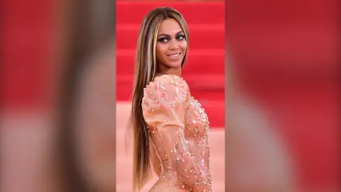 Beyonce wearing a pink dress stood in front of a red background