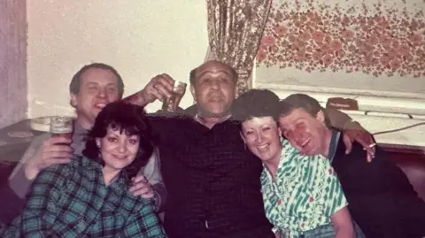 Family photograph Roy Dickinson (far right) and his wife pictured with Billy Boston (centre) in the star's pub, the Griffin Hotel, in the 80s. Another couple are in the picture to the left. They are all smiling.