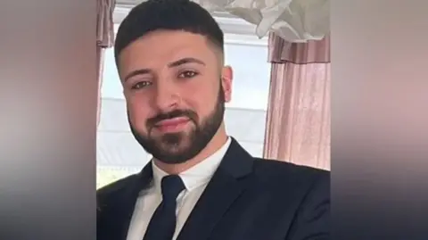 Hertfordshire Police Murder suspect Kyle Clifford with short black hair and a beard, wearing a suit.