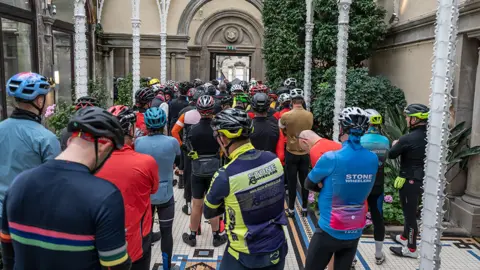 Ian Knight / Z70 Photography A group of cyclists in colourful kit, backs towards camera, inside Sandon Hall, listening to instructions