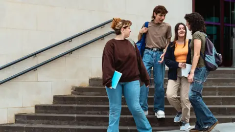 Four university students are having a conversation as they walk down the steps outside a university building