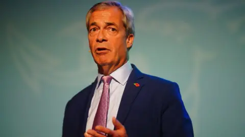 PA Media A grey-haired man with an orange complexion, wearing a dark blue suit and purple ties, stands in front of a light blue background 