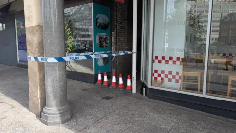 Police tape sealing a narrow alleyway between two shop frontages