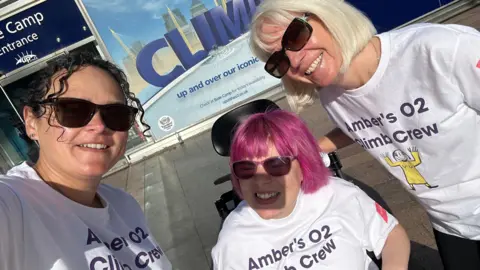 Contributed Another selfie of Amber Donovan, Kayleigh Jennings and another woman outside the 02 Arena. Ms Donovan has pink hair in the style of a bob and wears sunglasses. Ms Jennings has black curly hair and wears sunglasses. They all wear white T-shirts that read Amber's 02 Climb Crew.