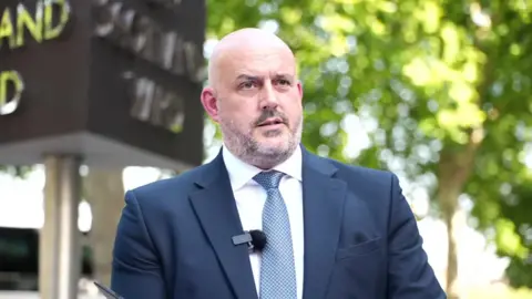 Laurence Taylor outside New Scotland Yard, wearing a navy blue suit and tie