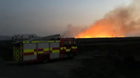 Charles Heslett/BBC Fire engine with glowing flames in background on horizon